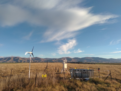 photo of eddy covariance system at a bit of a distance with pasture behind, mountains on the horizon with partly cloudy sky