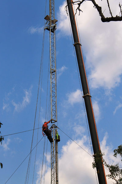a crane lowers the top part of the tower on to the guyed bottom part, while a rigger at the top of the first part guides the two parts together