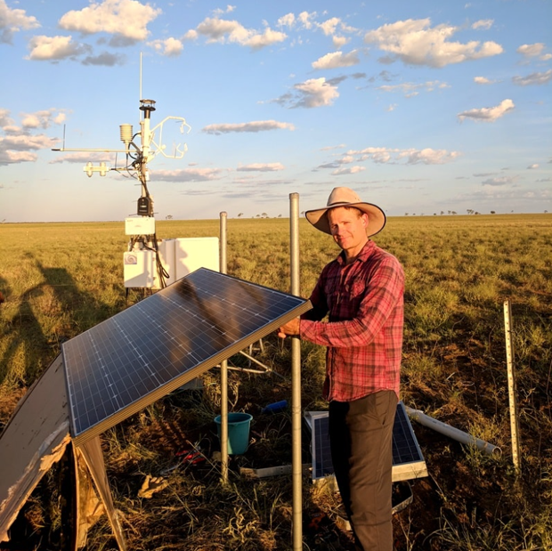 David Rowlings near solor panels with flux station of Mitchel Grass Ranglands site int he background
